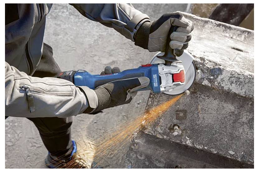 A person wearing gloves uses an angle grinder to cut a rough concrete block, causing orange sparks to fly outward.