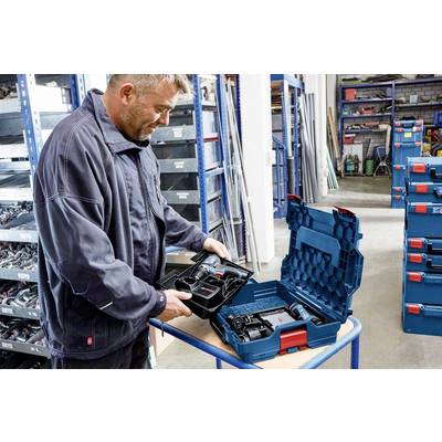 A man in workwear is checking drills in an open toolbox within a storage room with shelves full of additional toolboxes.