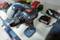 Cordless drill and accessories on a table. Additional tools blurred in the background. Dominant colour blue with red accents.