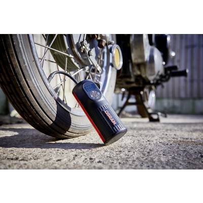 A portable tyre compressor next to a motorcycle tyre is inflating the tyre. The display shows 0.00 psi. The sun is shining on the scene.