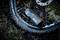 A portable compressor is pumping up a bicycle tyre. The display reads '0.00'. The surrounding environment is damp forest floor.