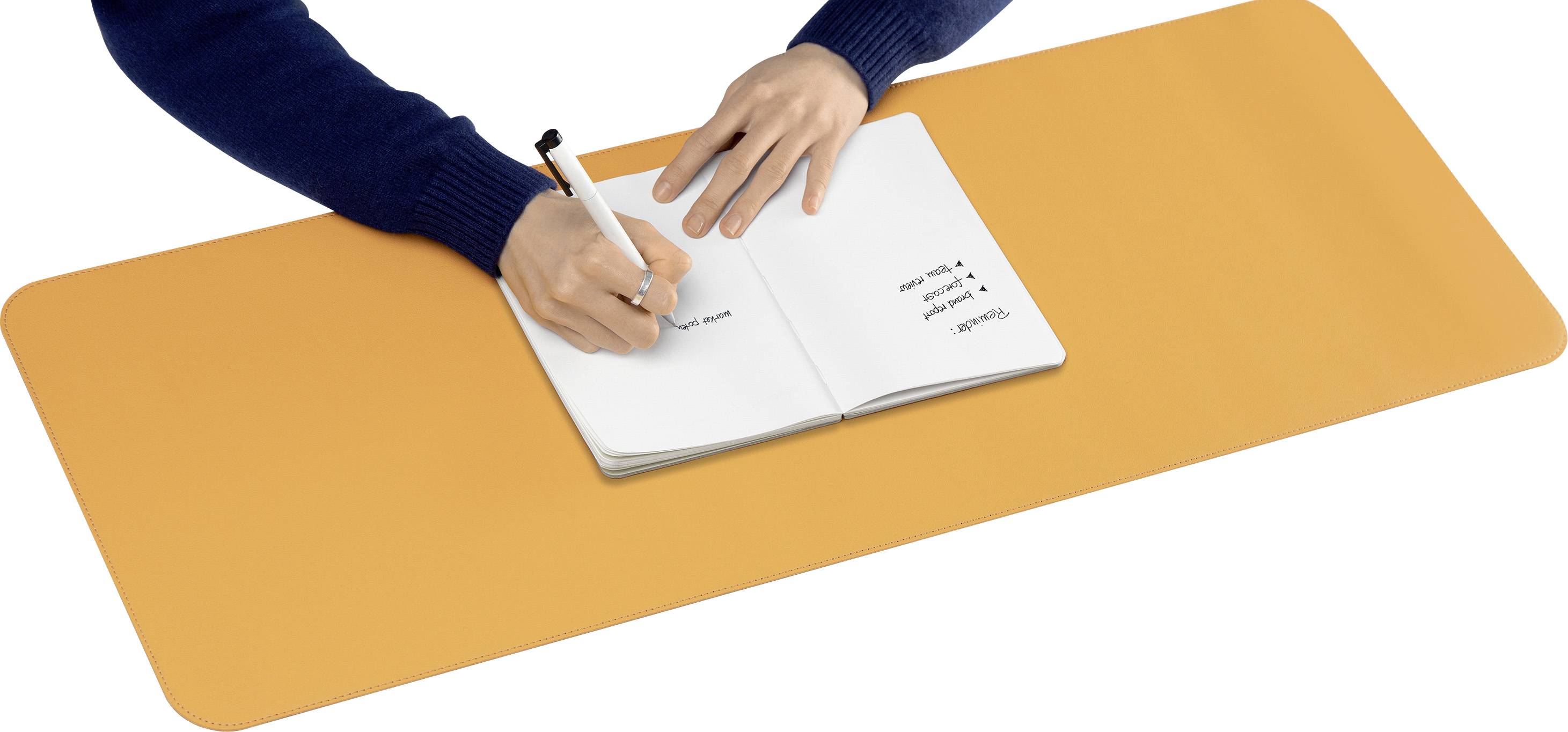 A person is writing with a pen in a notebook on a large, orange desk mat.