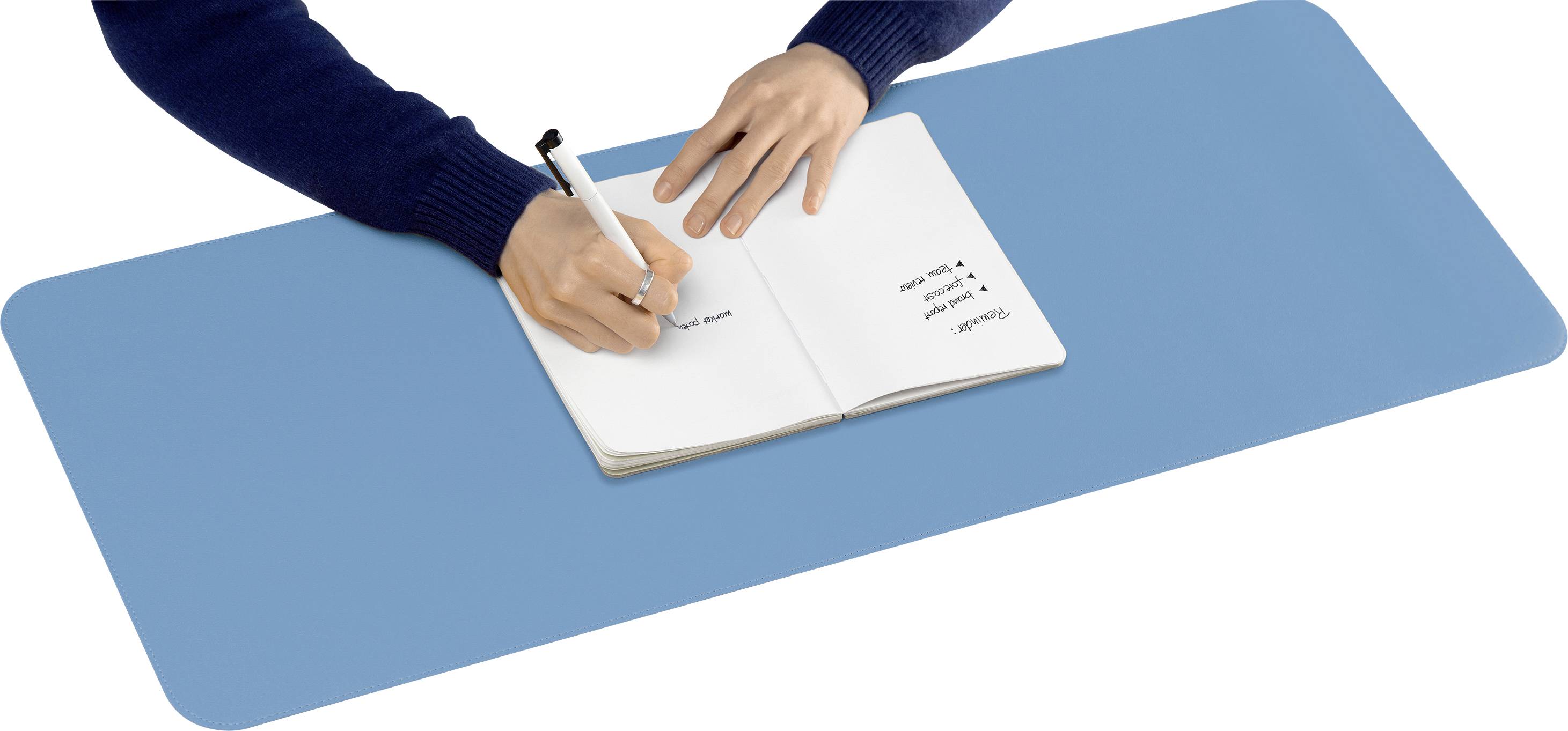 A person is writing in a notebook that is resting on a blue desk mat. The page contains handwritten notes.