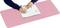 A person is writing with a pen in a notebook on a large pink desk mat.