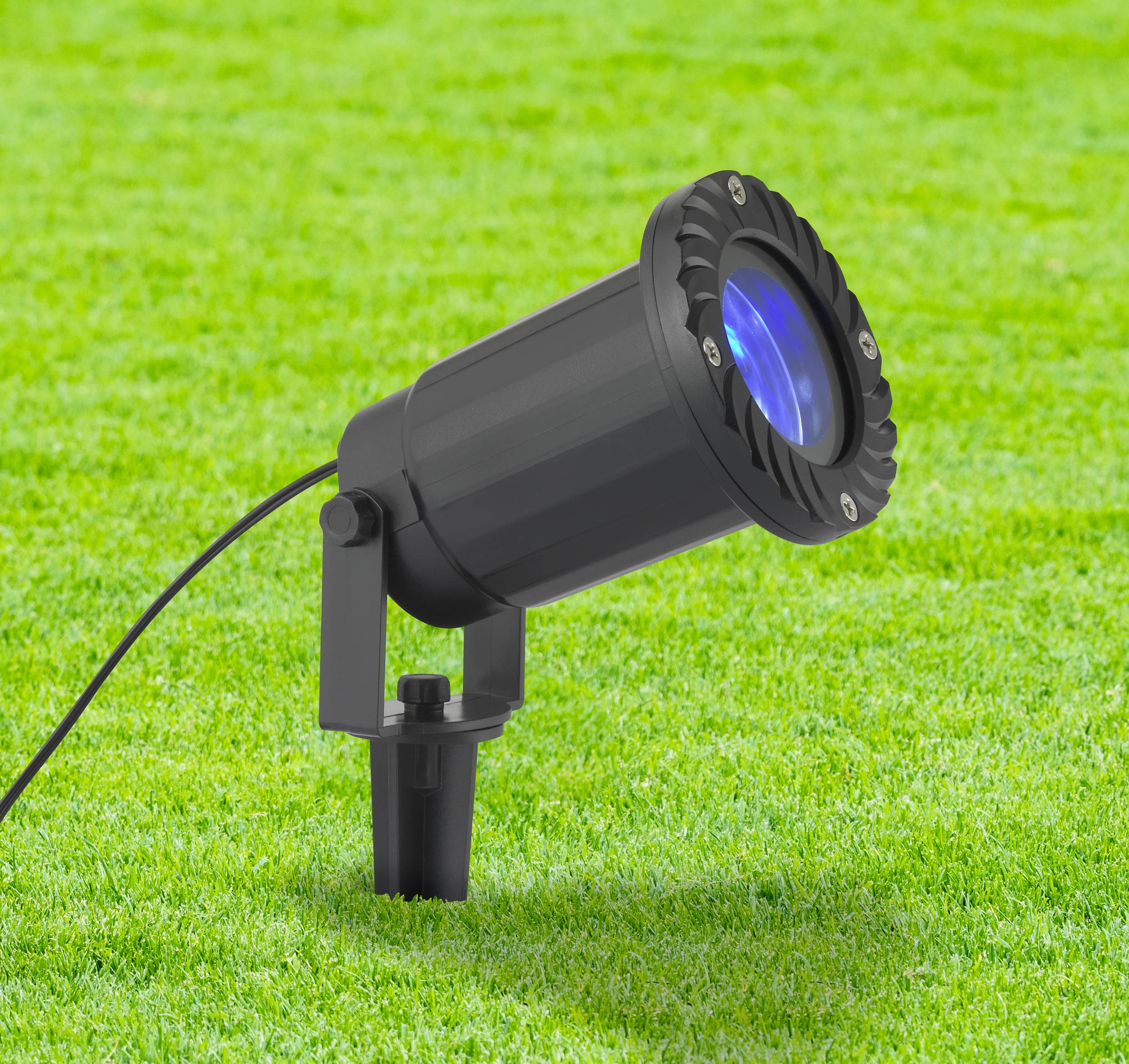 A black garden spotlight with blue light is standing on a lawn and is pointing upwards.