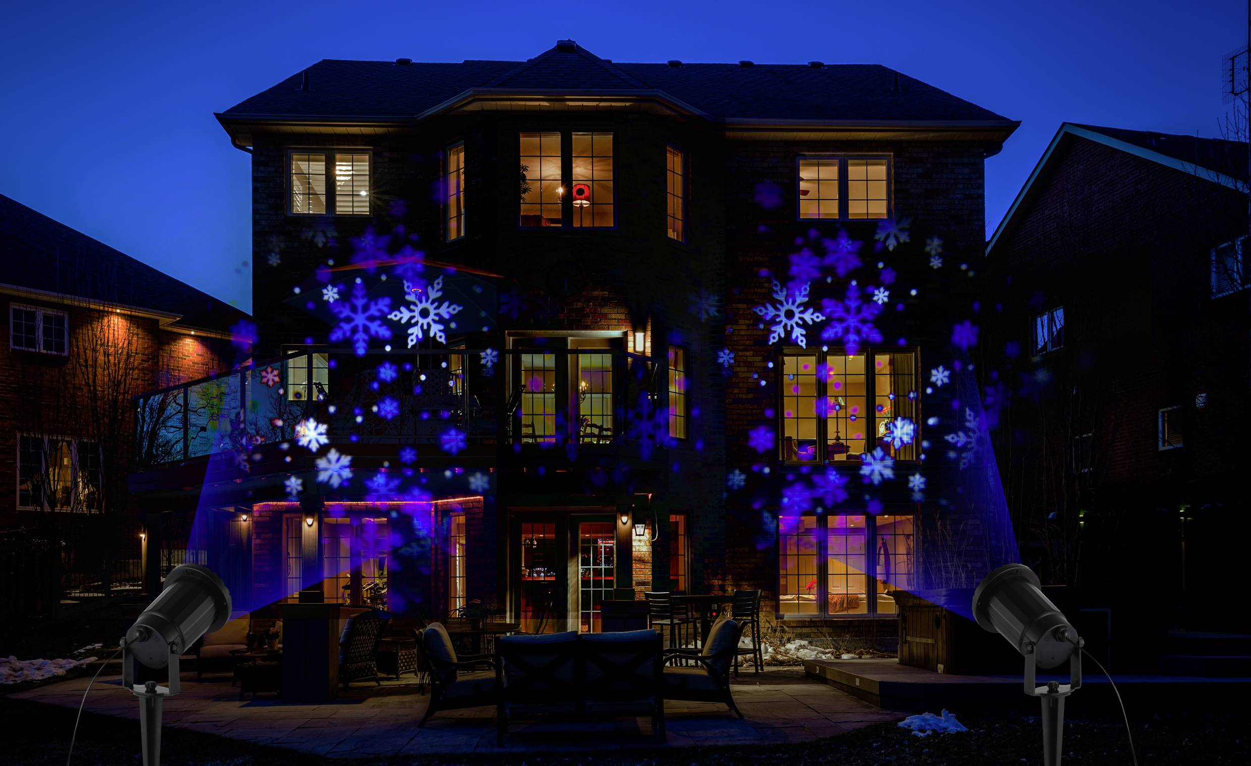 House facade at night, illuminated by colourful, projected snowflake patterns from two spotlights in the foreground.