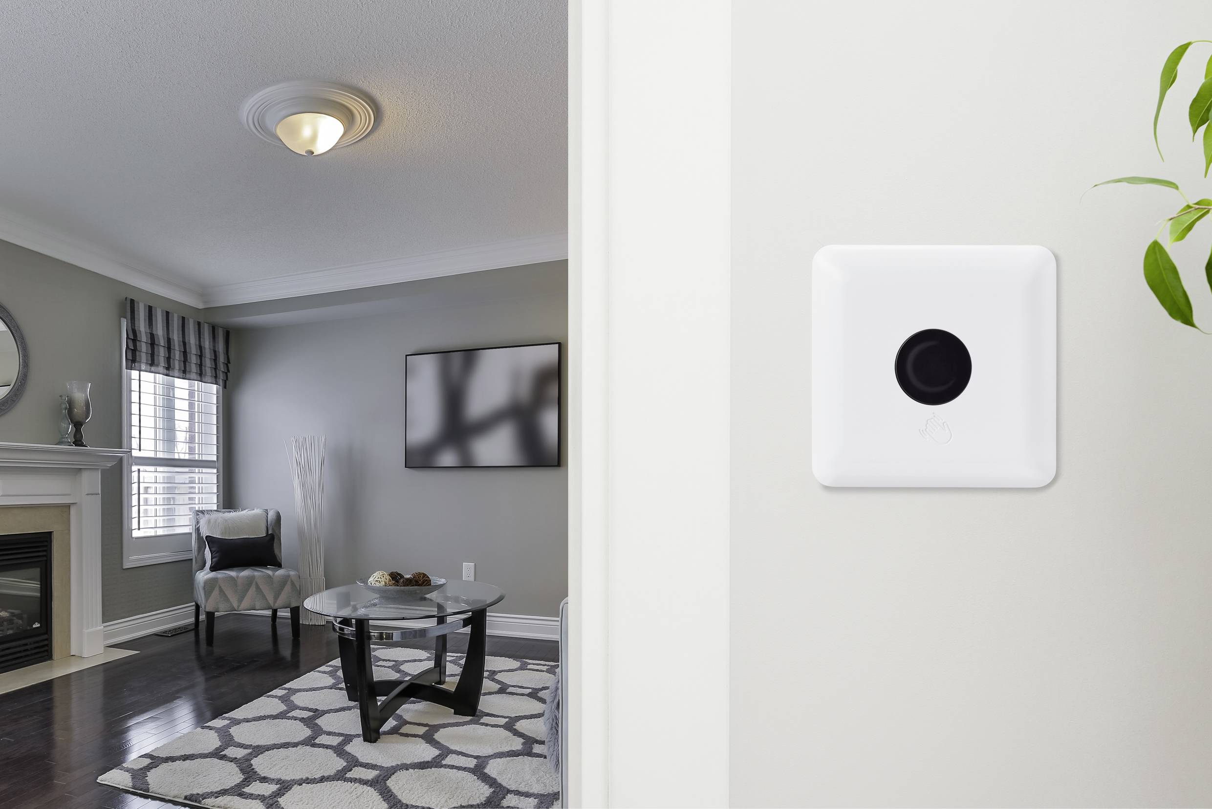 A light switch on a white wall, with a modern living room in the background featuring grey walls, a fireplace, an armchair, and a glass coffee table.