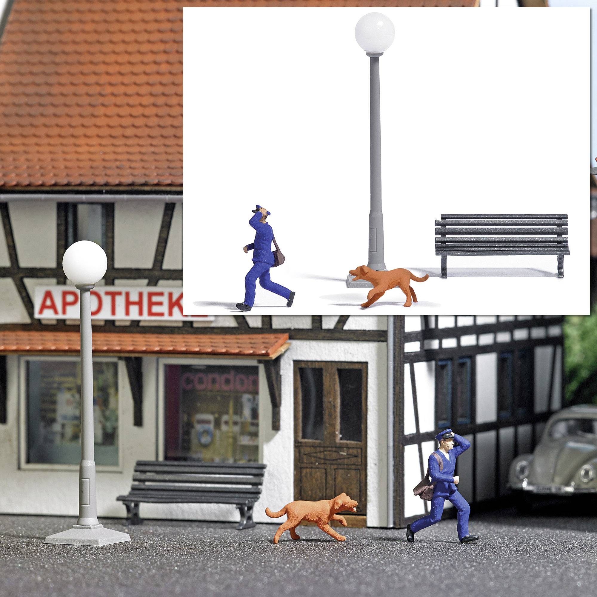 A miniature model shows a street lamp, a bench, and a man walking a dog in front of a half-timbered house with a pharmacy on its facade.
