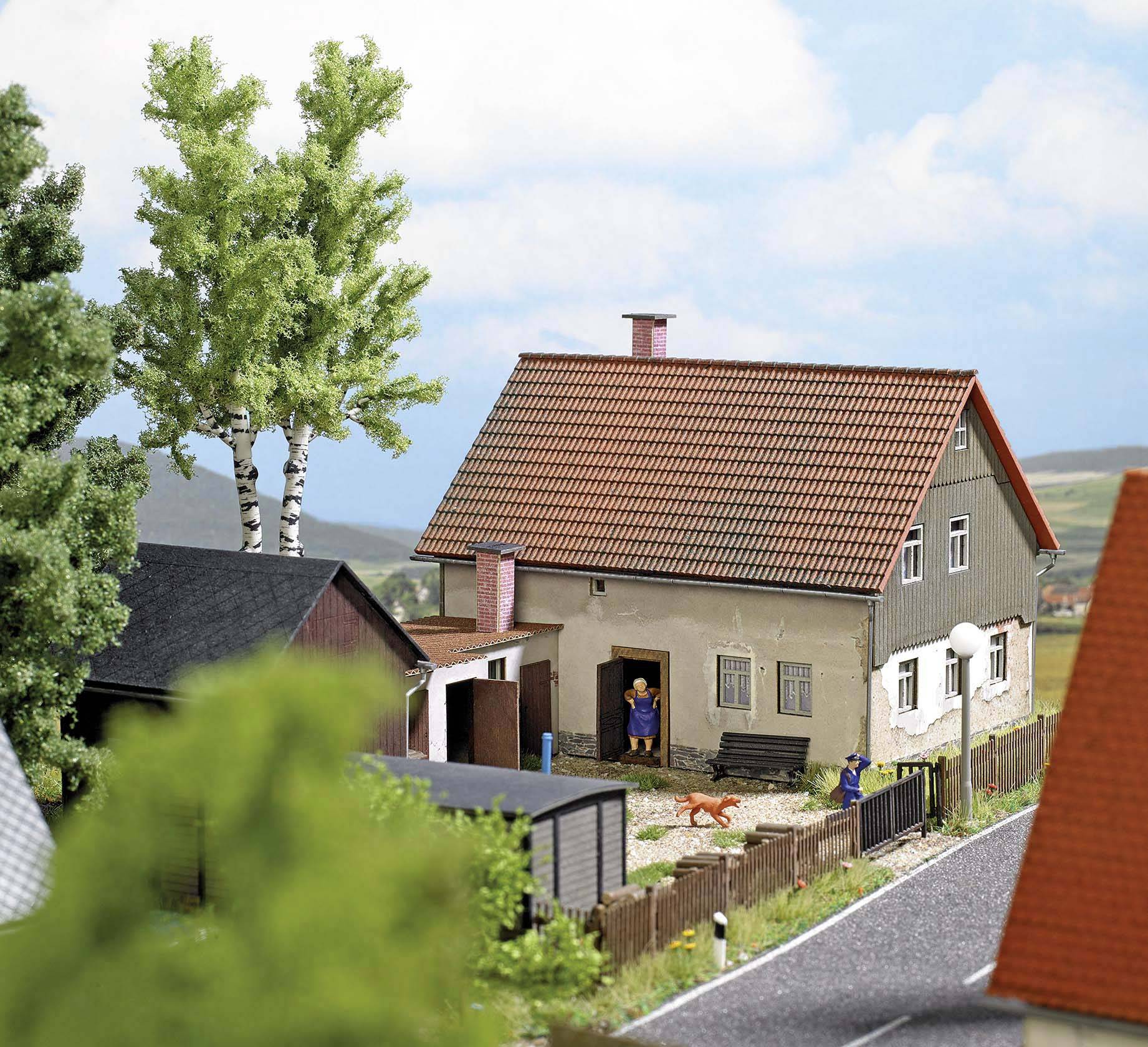 A rural scene depicts a house with a red roof, surrounded by trees and a fence. Two people are standing in the garden, with a dog running around.