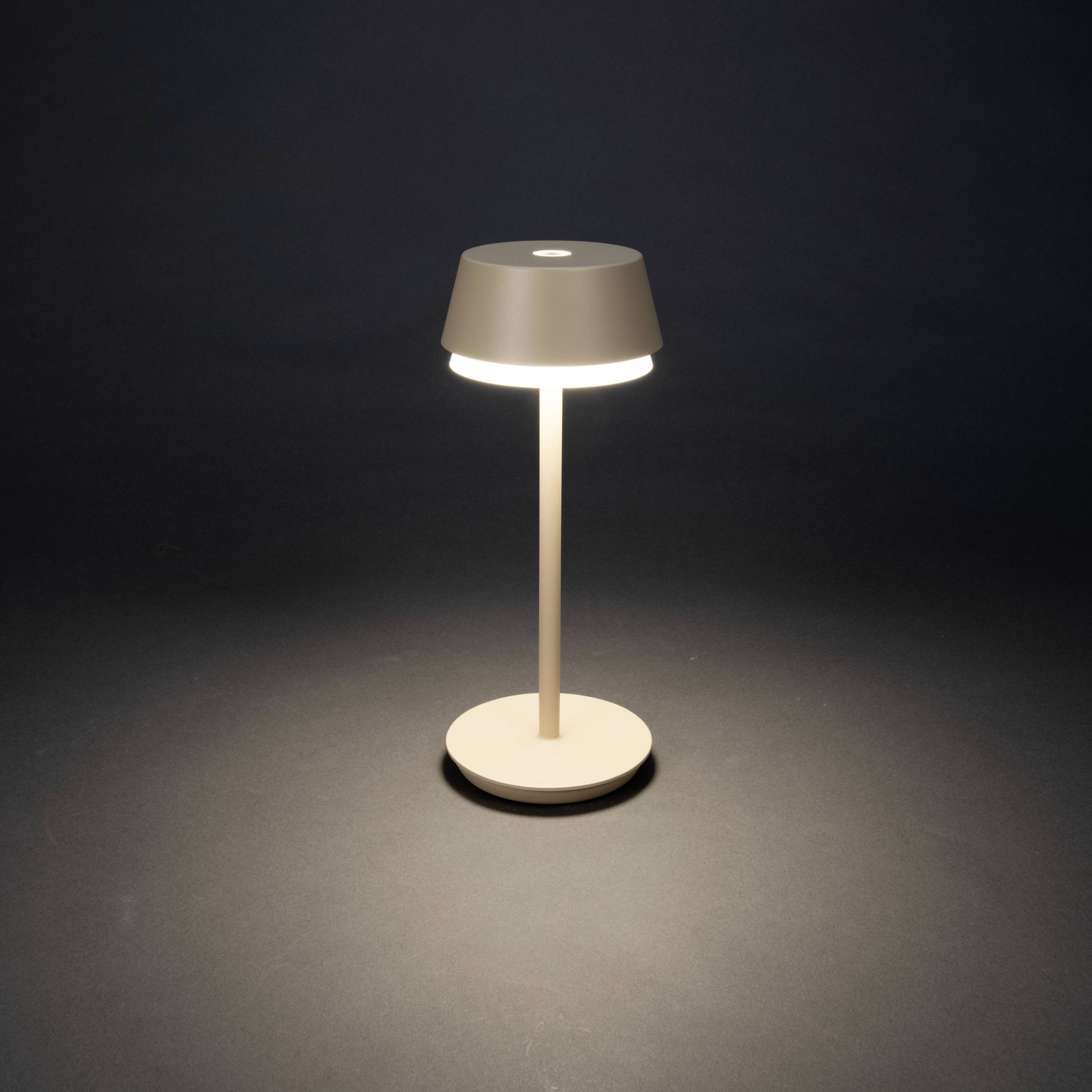 A modern, minimalist table lamp with a round shade emits warm light onto a dark surface.