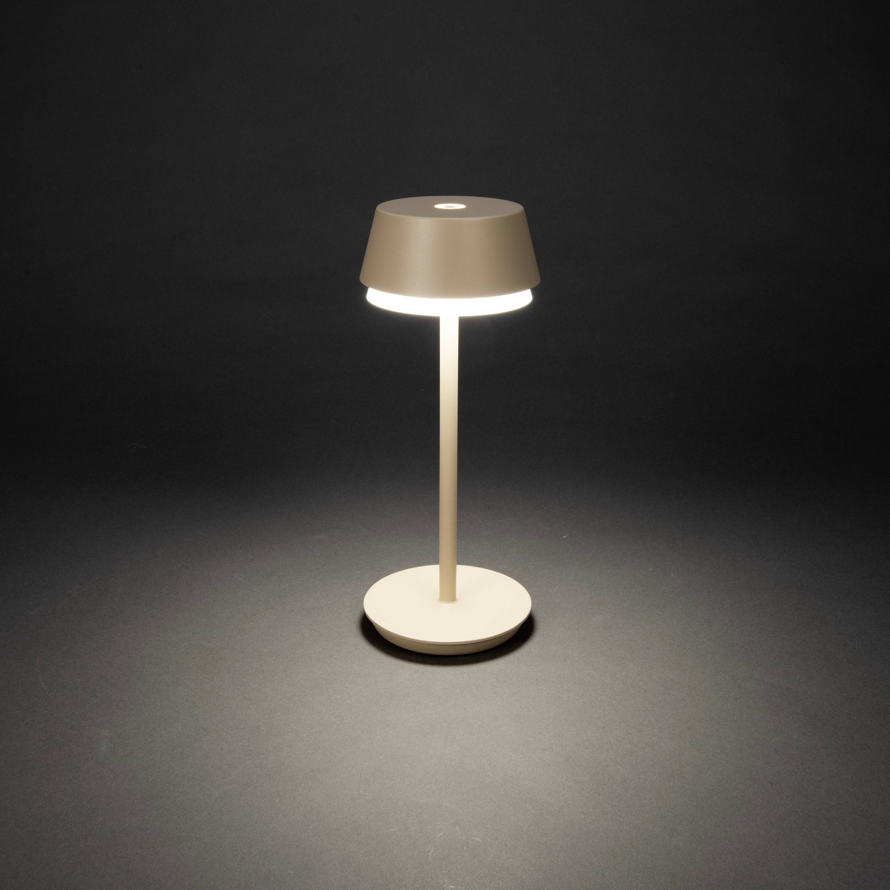 A modern table lamp with a round shade and minimalist design is switched on and illuminating the surroundings with warm light.