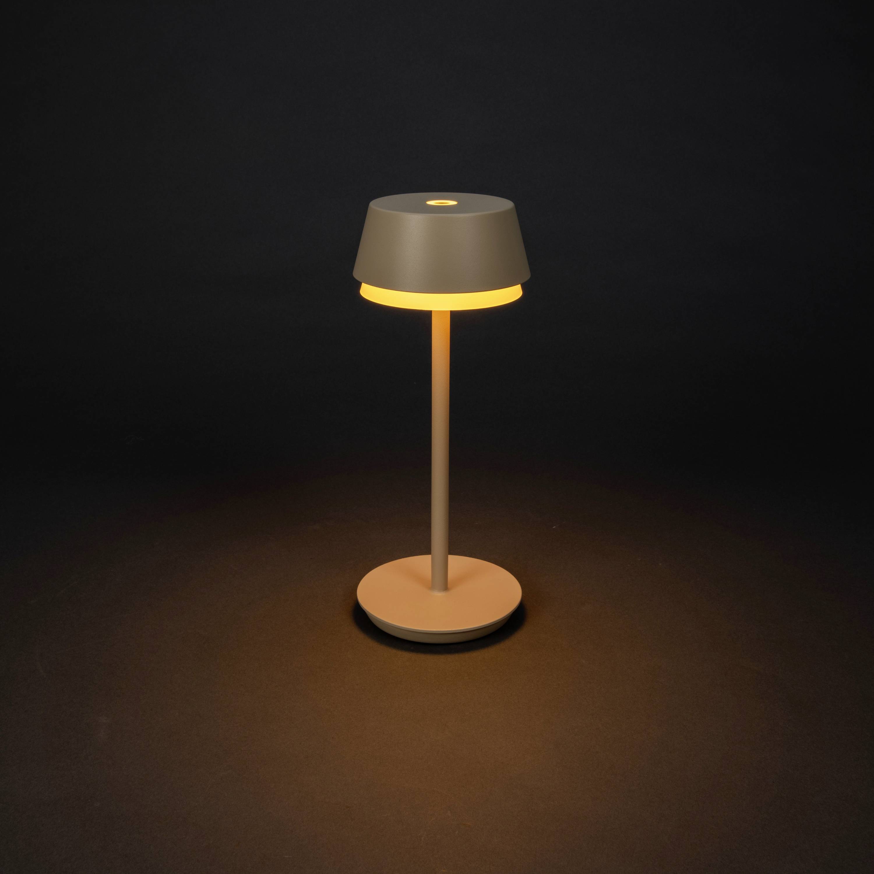 A minimalist table lamp with a round base and shade glows warmly against a dark background.
