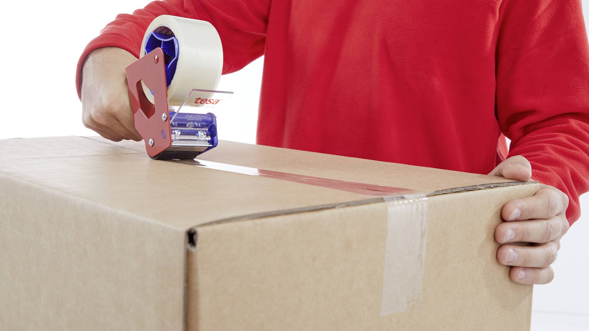 A person is sealing a cardboard box with parcel tape. She is wearing a red top. The box is being prepared for dispatch.