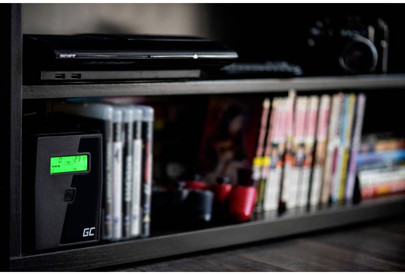 A shelf with a games console, video games, manga and a small electronic device with a green display.