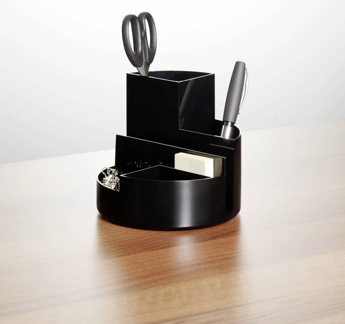 Black, round desk organiser with scissors, pen, paperclips, and sticky notes on a wooden table.