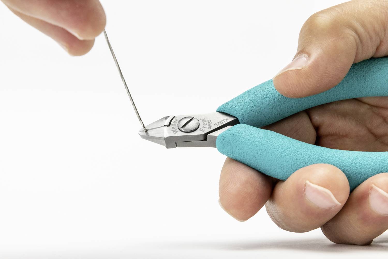 A hand is holding pliers with turquoise handles, cutting through a thin wire.