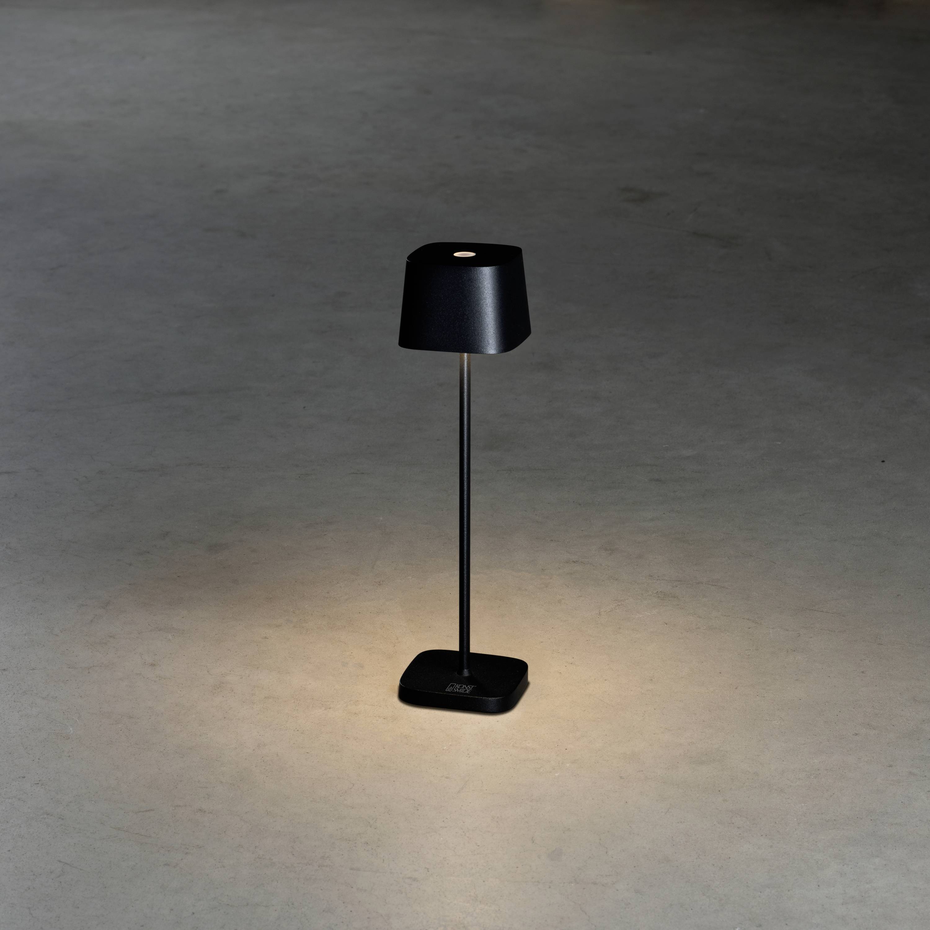 Black standing lamp on a smooth floor, casting warm light downwards. Modern, minimalist style.