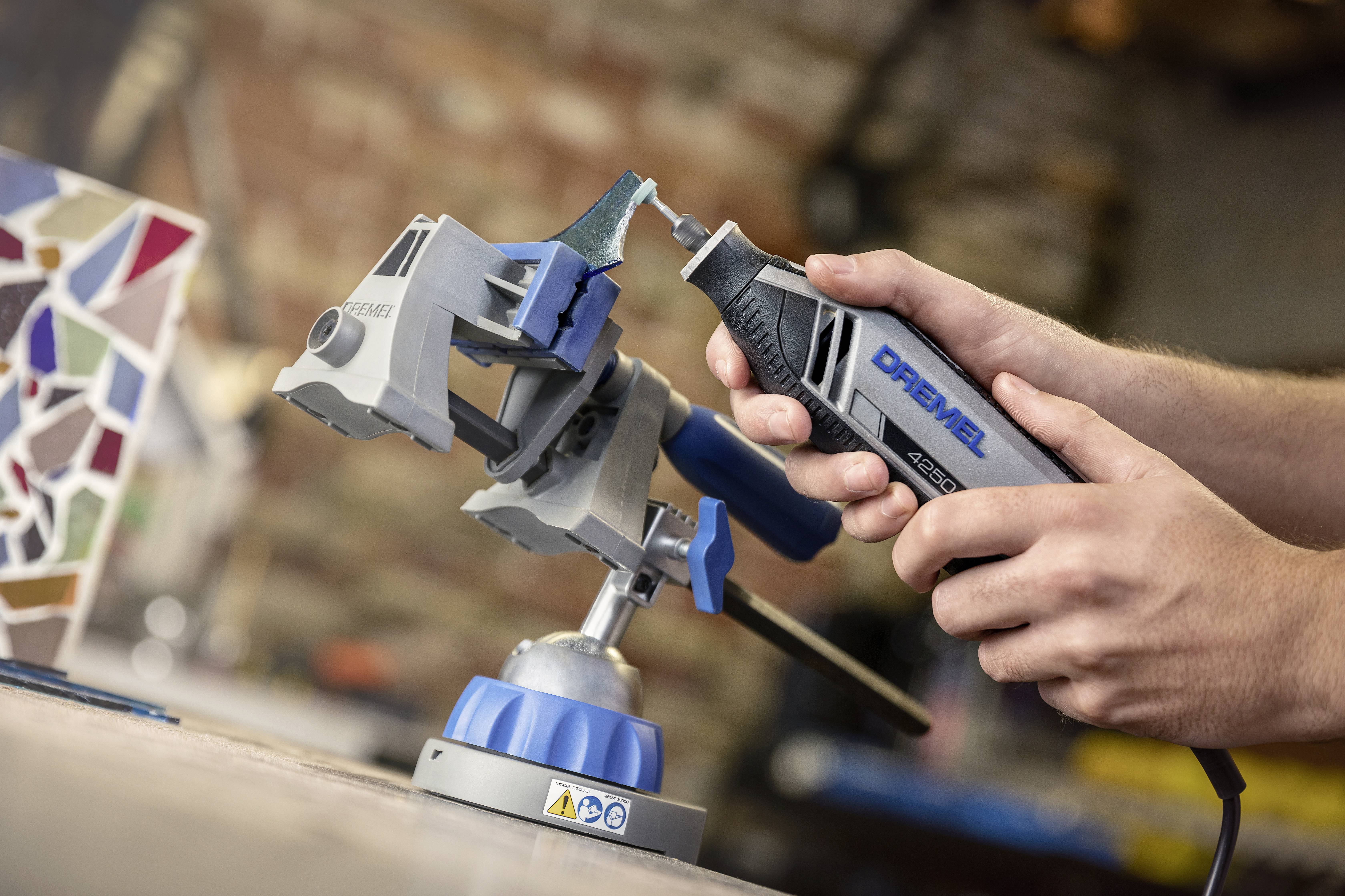 A person is using a rotating tool on a workpiece clamped in a vice. Workshop environment.