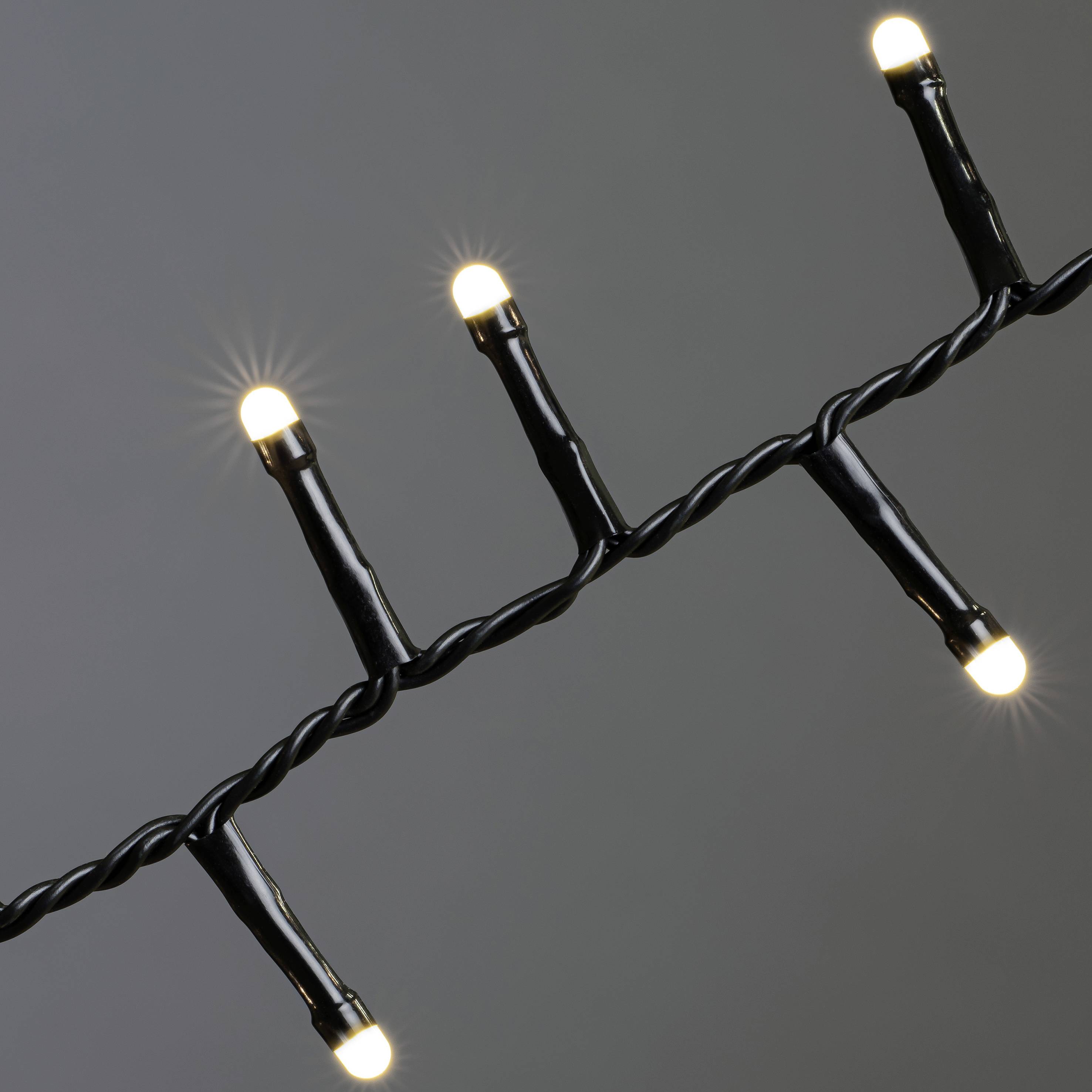 A string of lights with multiple glowing white bulbs, evenly distributed along a black cable, against a grey background.
