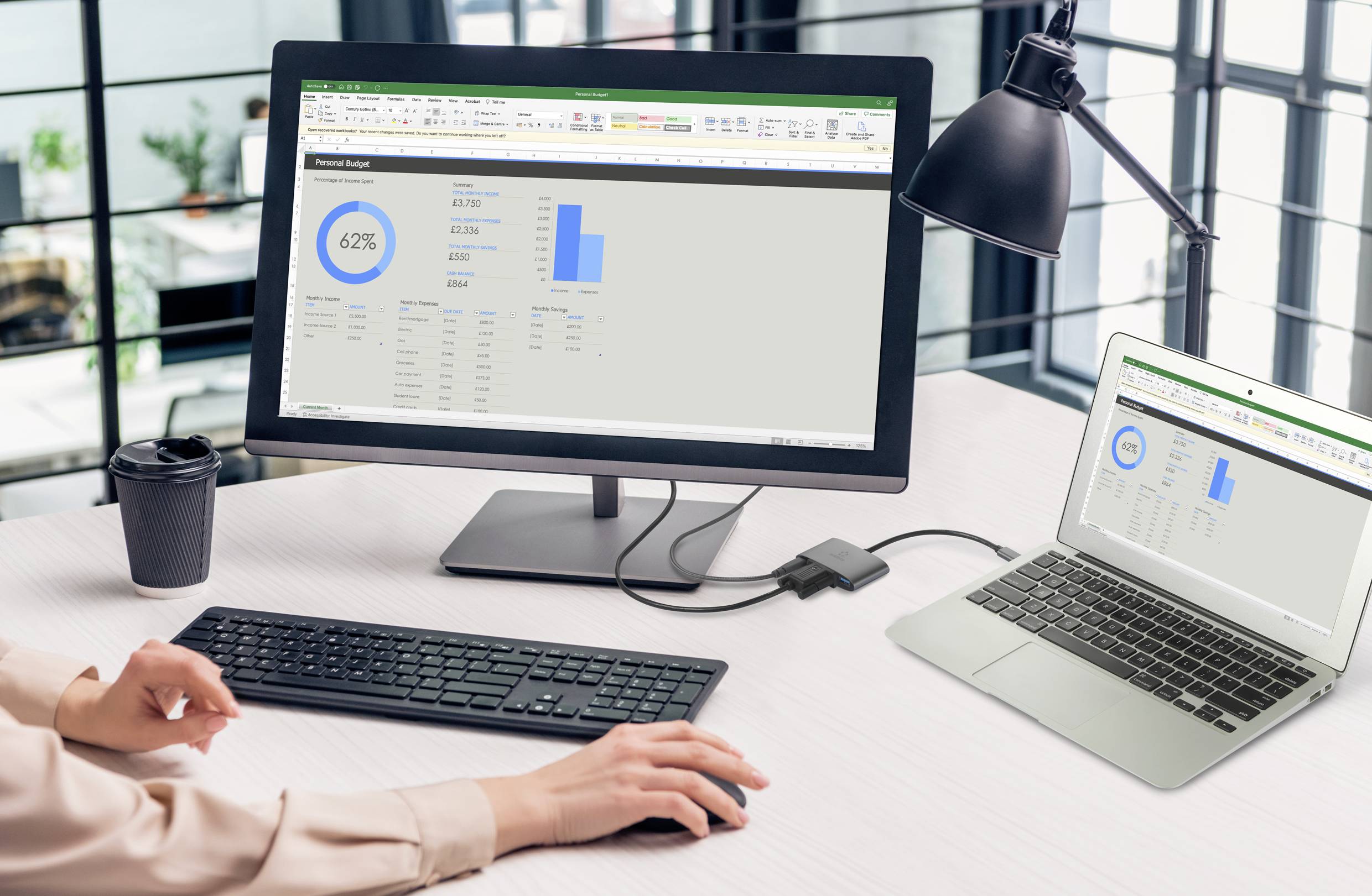 A person is working on a laptop and computer with a financial diagram displaying bar charts and percentages in an office.
