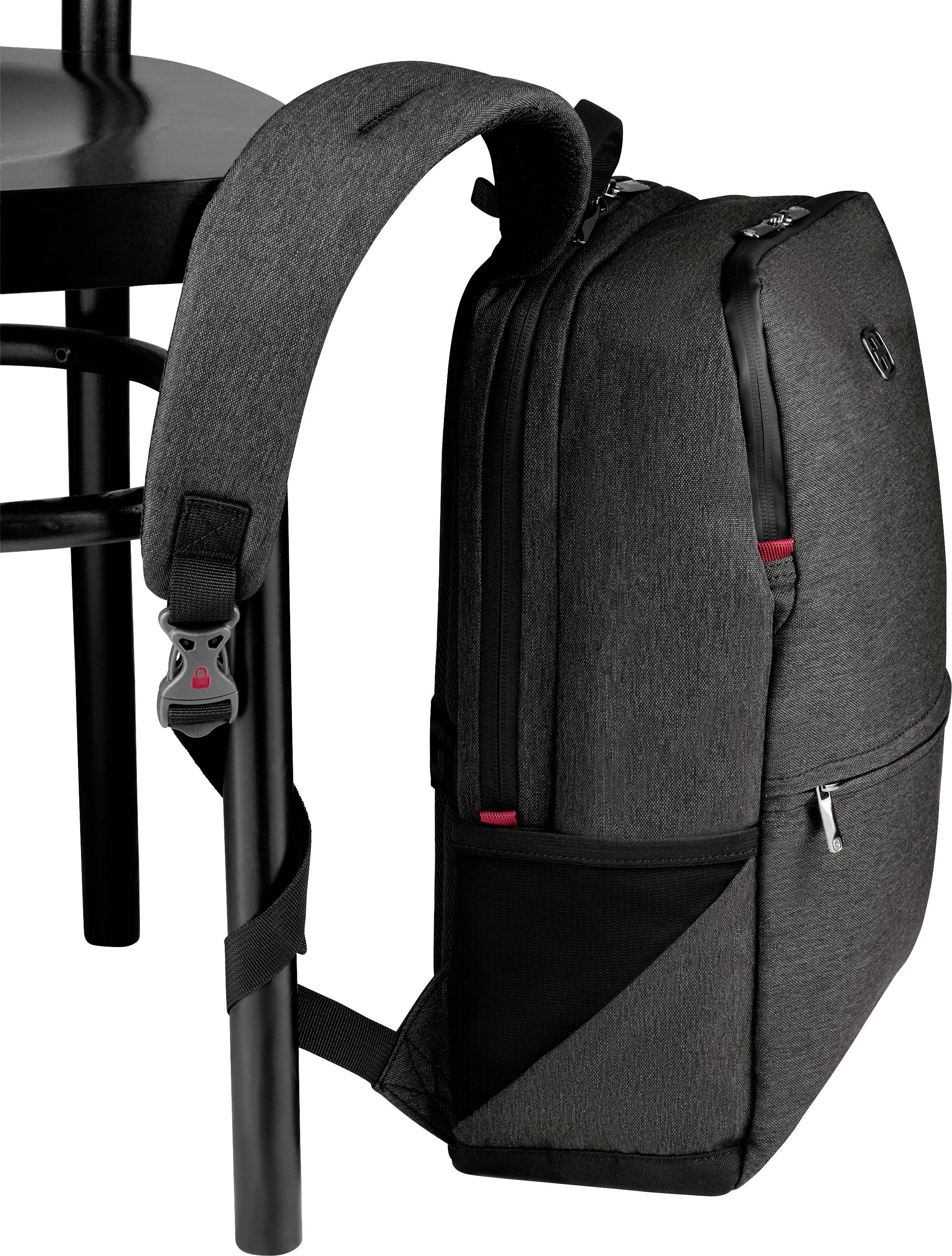 A dark grey fabric rucksack is hanging on a chair back. It has multiple zips and side pockets.