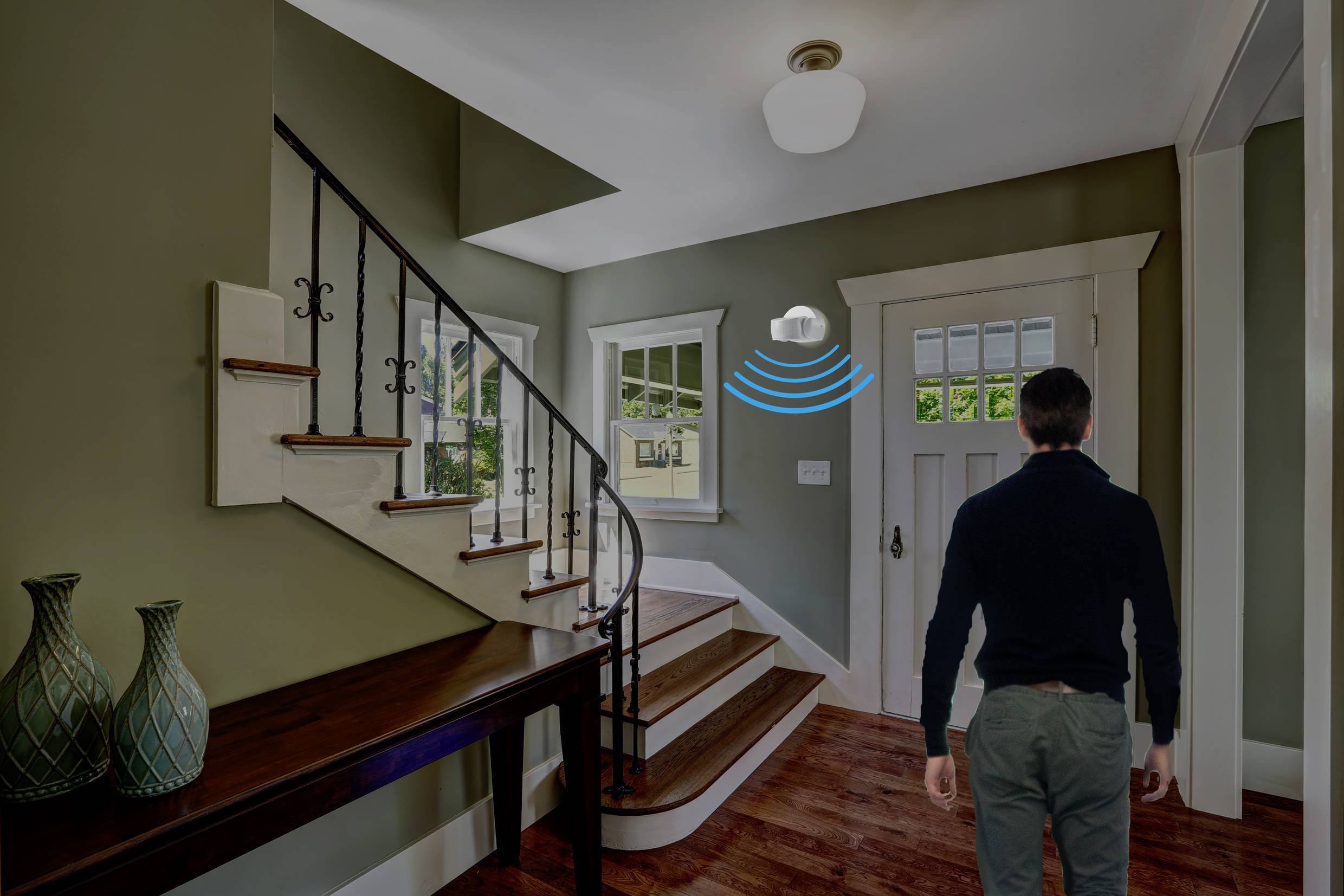 A man enters a corridor with a staircase. A motion sensor is fitted to the ceiling and is active.