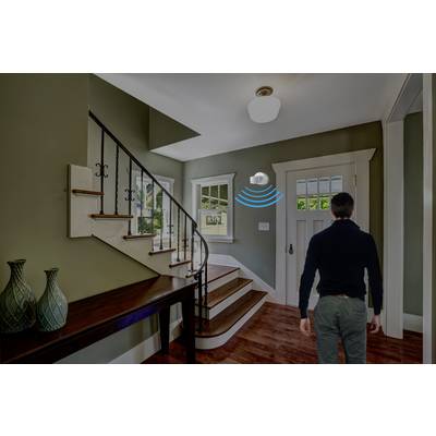 A man enters a corridor with a staircase. A motion sensor is fitted to the ceiling and is active.