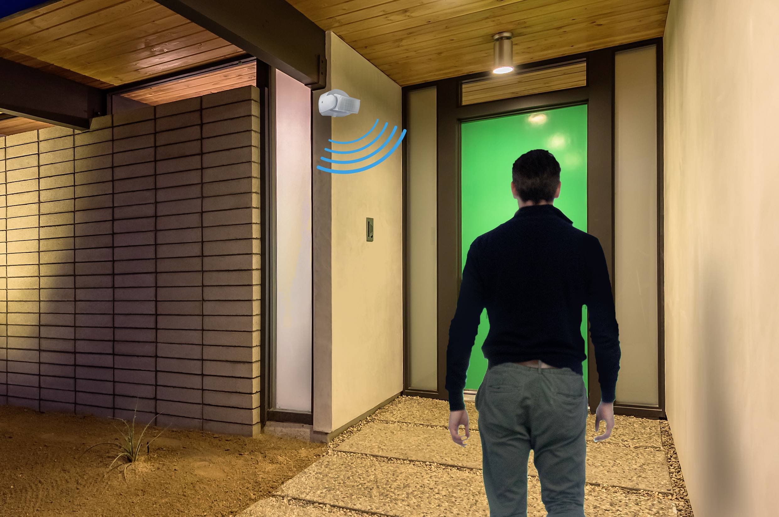 A person approaches a front door with green light, while a motion sensor is activated and depicts waves.
