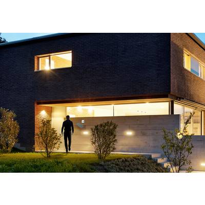 A modern house at dusk. A person walks along an illuminated path, surrounded by a minimalist garden landscape.