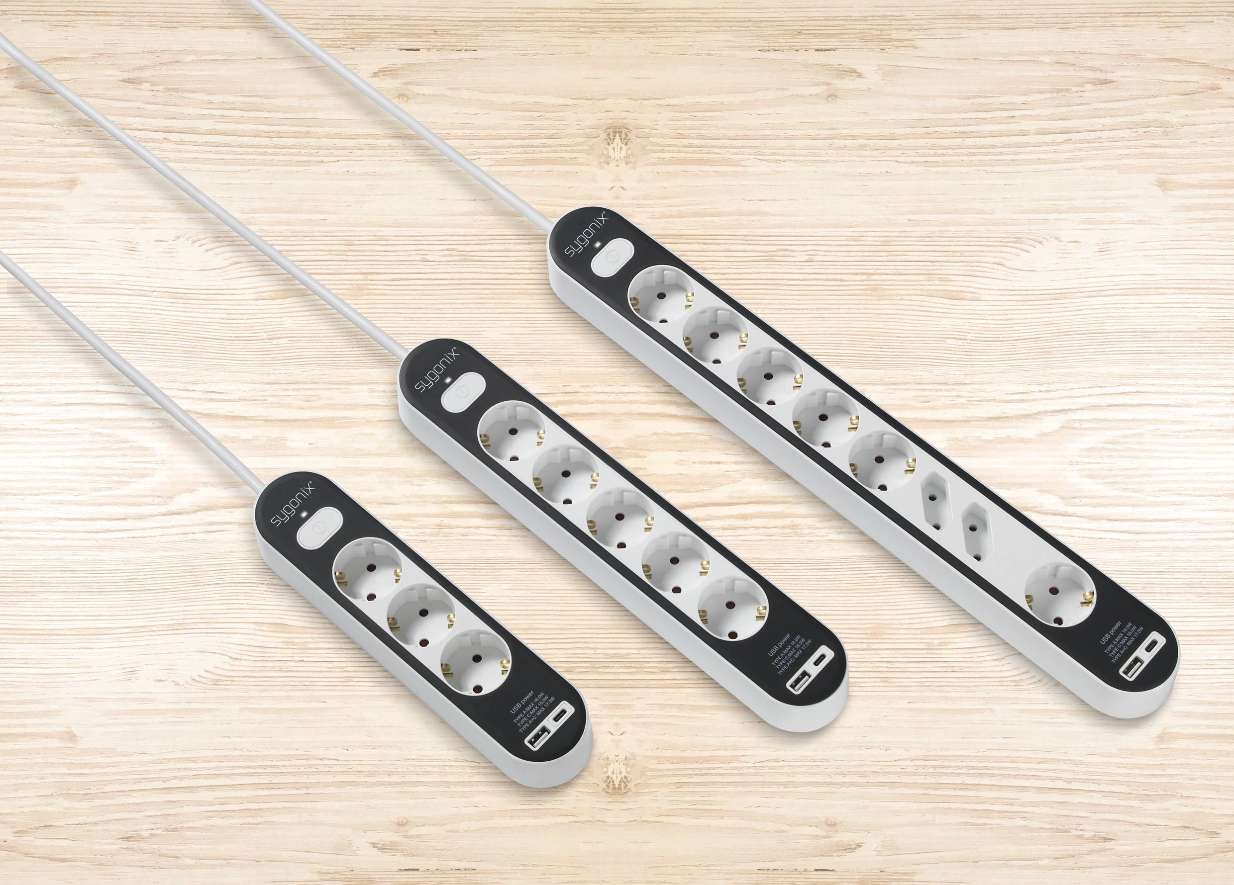 Three power strips, each with multiple sockets and an on/off switch, are lying side by side on a wooden table.
