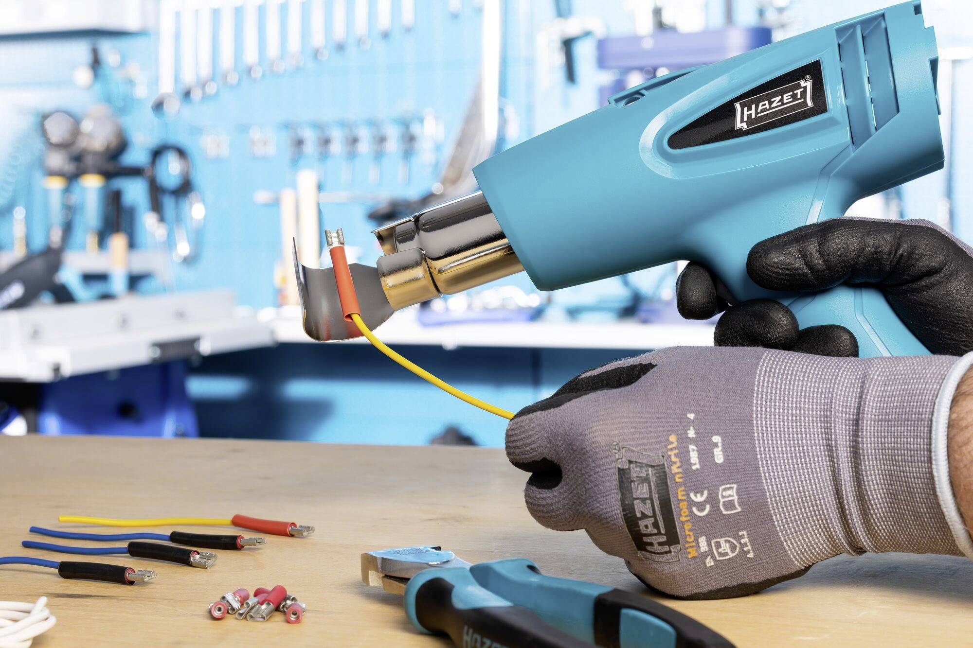'Worker uses hot air gun to work on cables at the table. Tools and cables in various colours lie on the surface.'