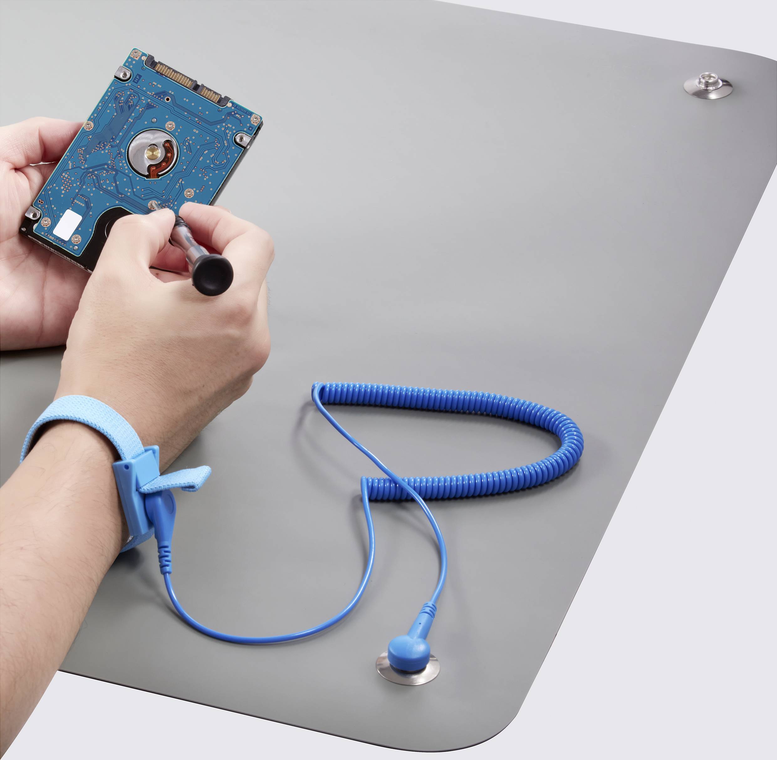 A person is repairing a hard drive with a screwdriver. They are wearing an anti-static wristband to prevent damage from static electricity.