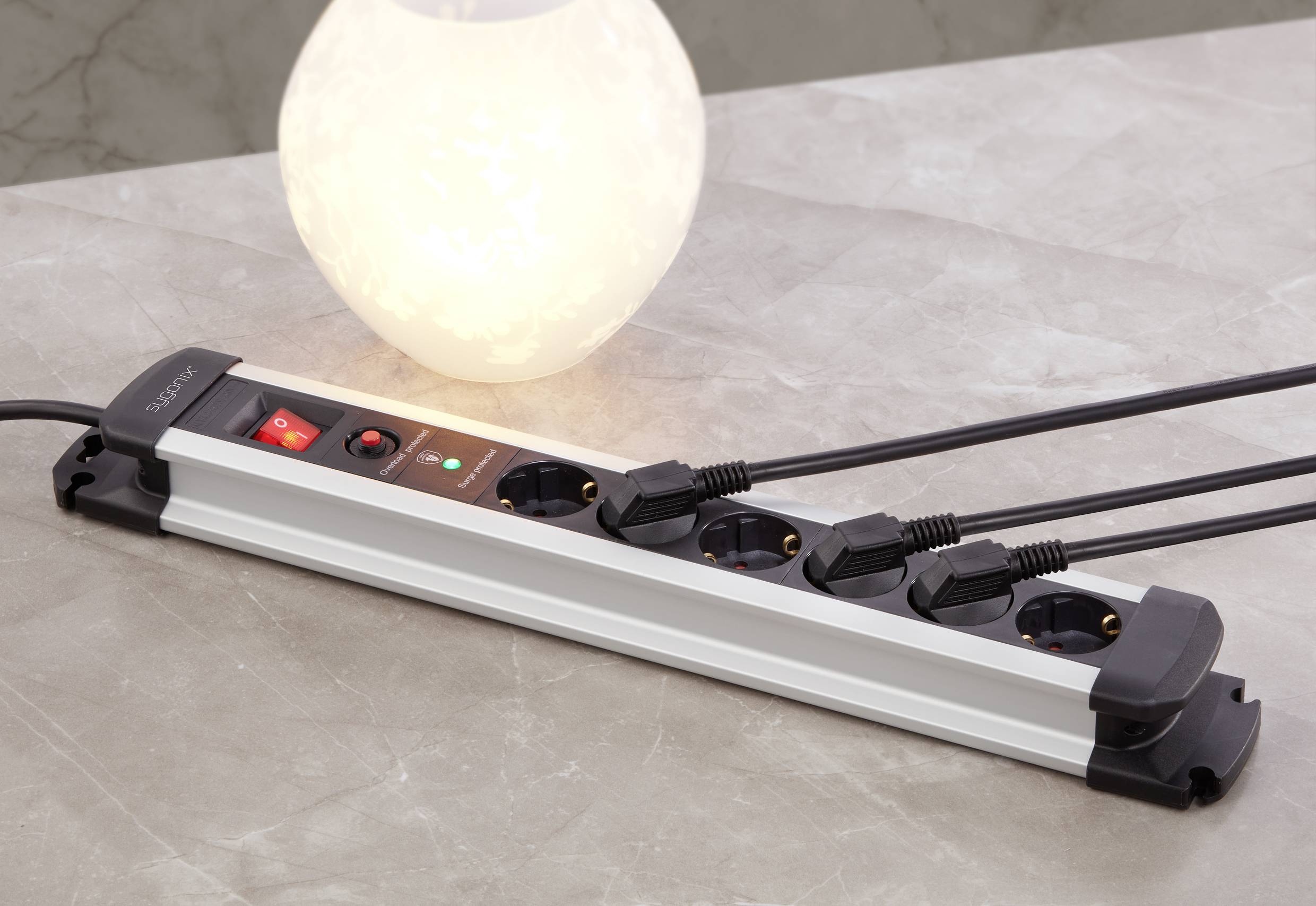 A multi-socket extension lead with five occupied plug sockets and an illuminated night light sitting on a table.