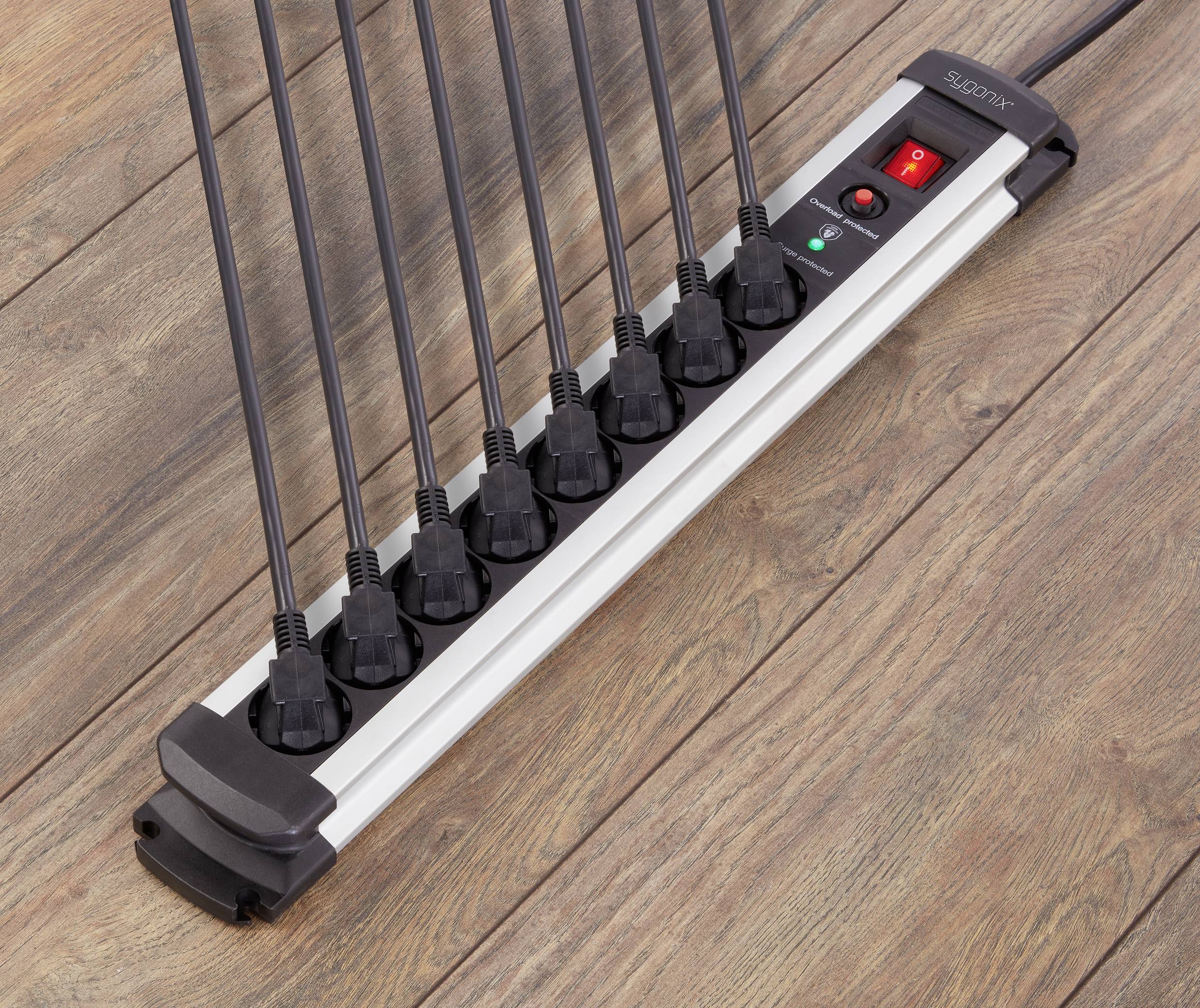 A multi-socket extension lead with eight black cables plugged in is resting on a wooden floor. A red on/off switch is visible.
