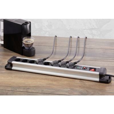 Multiple socket extension lead on a wooden table with six cables plugged in. In the background, a coffee machine with a cup stands.