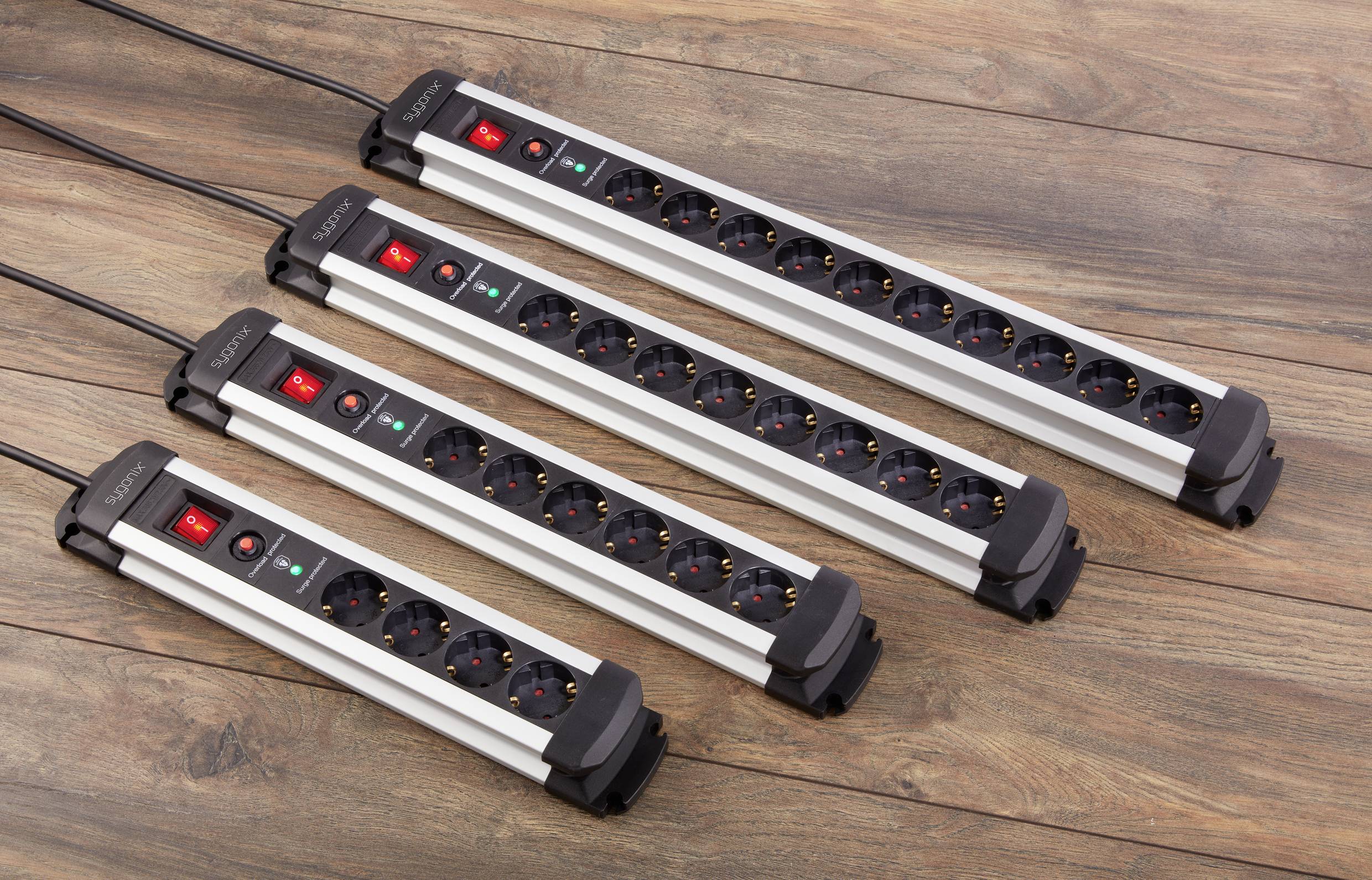 Four silver socket strips, each with five plug sockets and red on/off switches, are lying on a wooden floor.