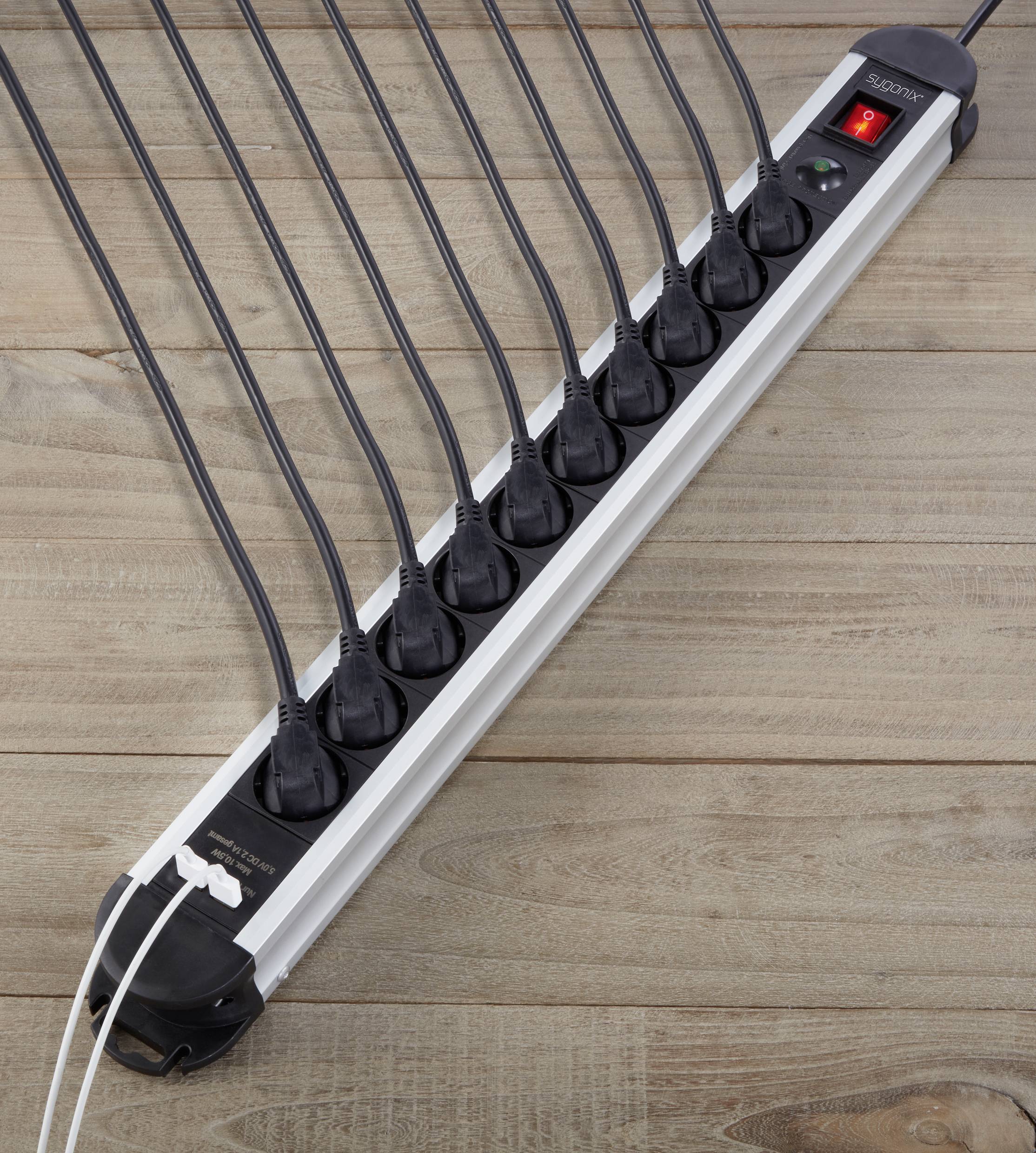 A multi-socket extension lead with a red switch, lying on a wooden floor. Several black cables are connected.