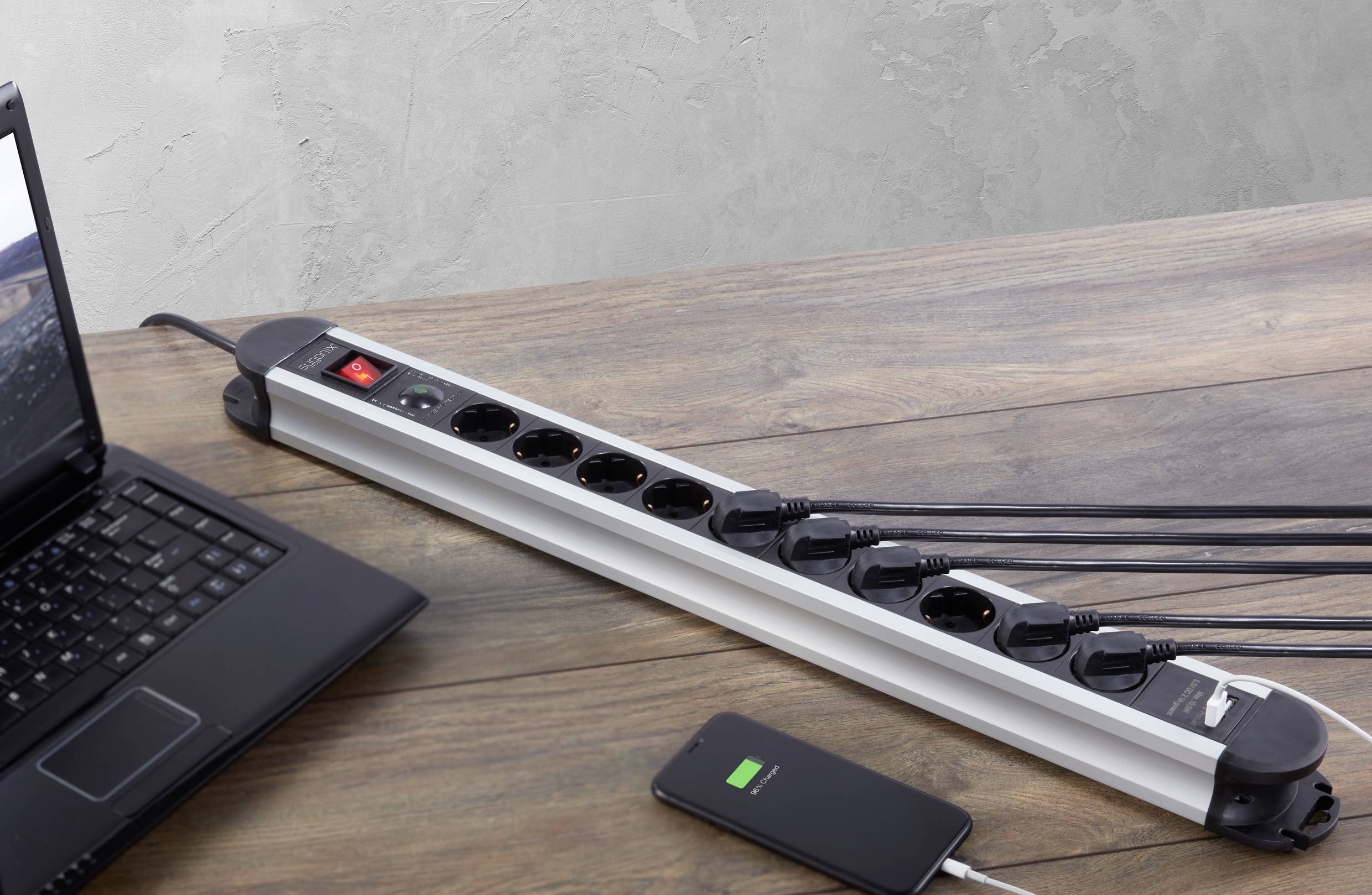 A laptop and a smartphone are connected to a multi-socket power strip with several cables plugged in. The laptop lid is open.