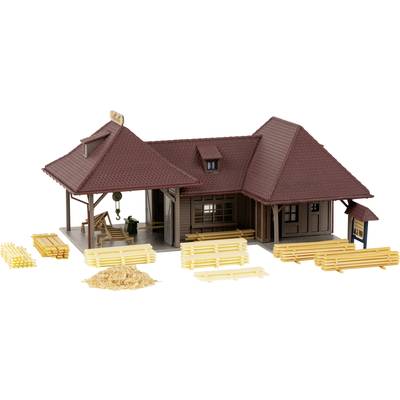 Miniature model of a rural railway station with wood piles in the foreground. The building has a tiled roof, sheds, and a heap of timber.