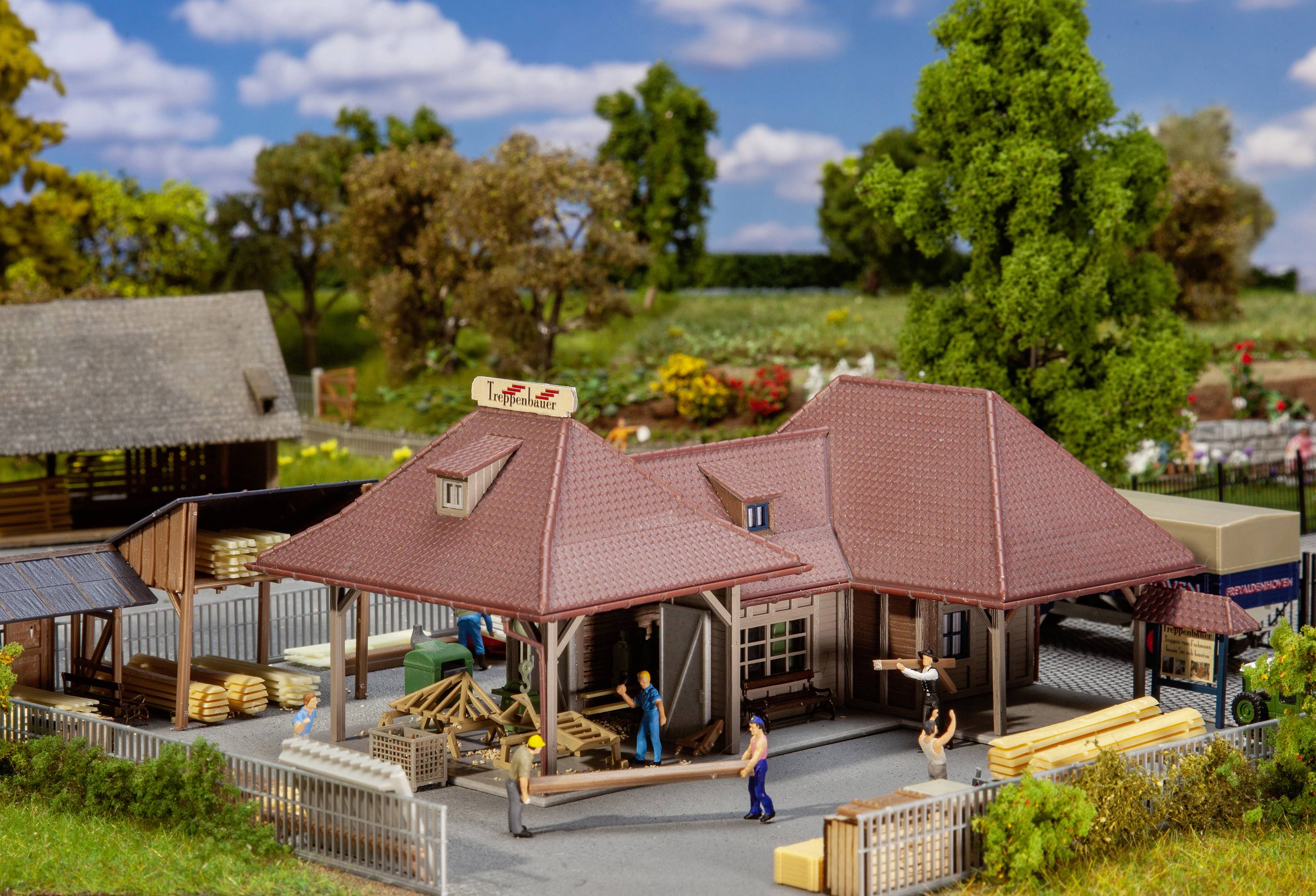 Miniature model of a woodworking scene: Workers carrying timber, buildings with red roofs, surrounded by trees and a fence.