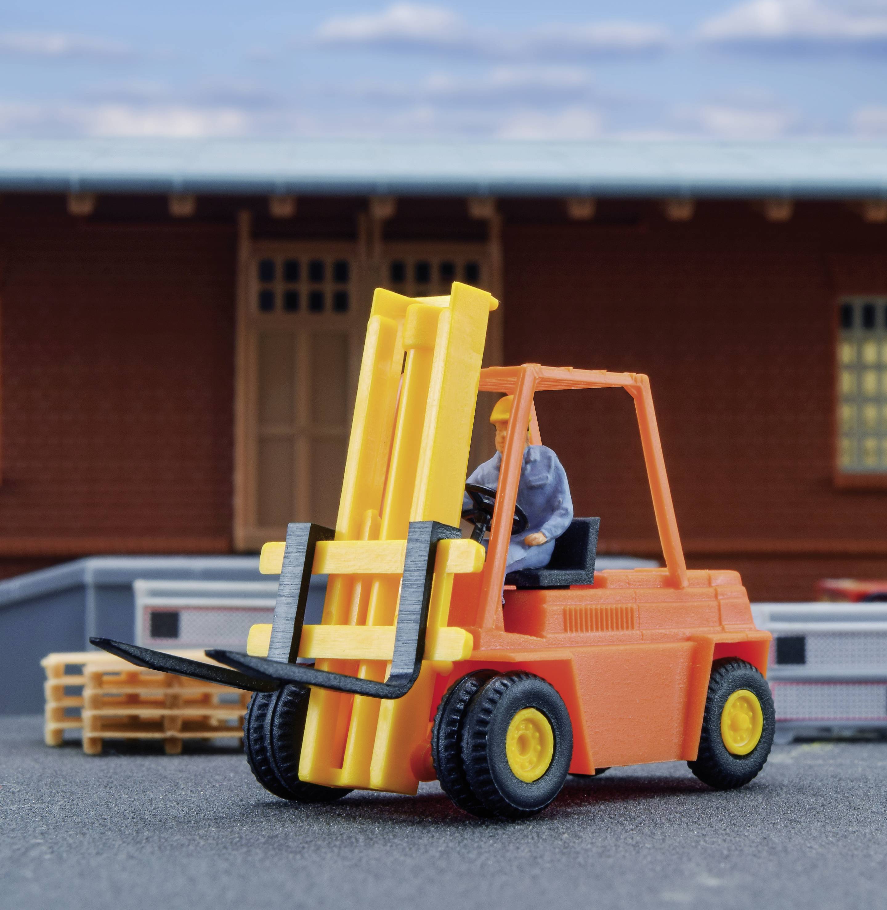 A small model of a forklift is lifting a pallet in front of a warehouse building. The sky is partly cloudy.