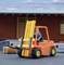 A small model of a forklift is lifting a pallet in front of a warehouse building. The sky is partly cloudy.