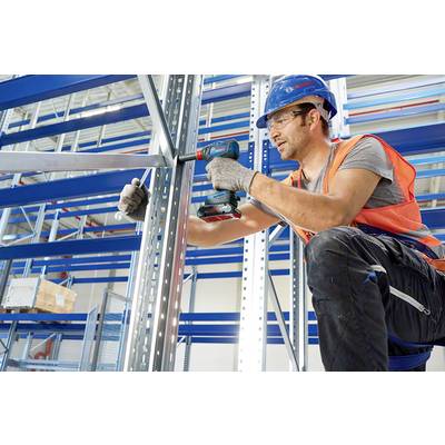 A worker in protective gear is assembling a metal shelving unit with a cordless drill in a warehouse.
