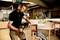 A man in a workshop is using a drill to work with wood. Tools and machines can be seen in the background.
