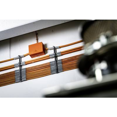 Orange cables run neatly along a wall. An orange box is attached to the cables. Metallic components are blurred in the foreground.