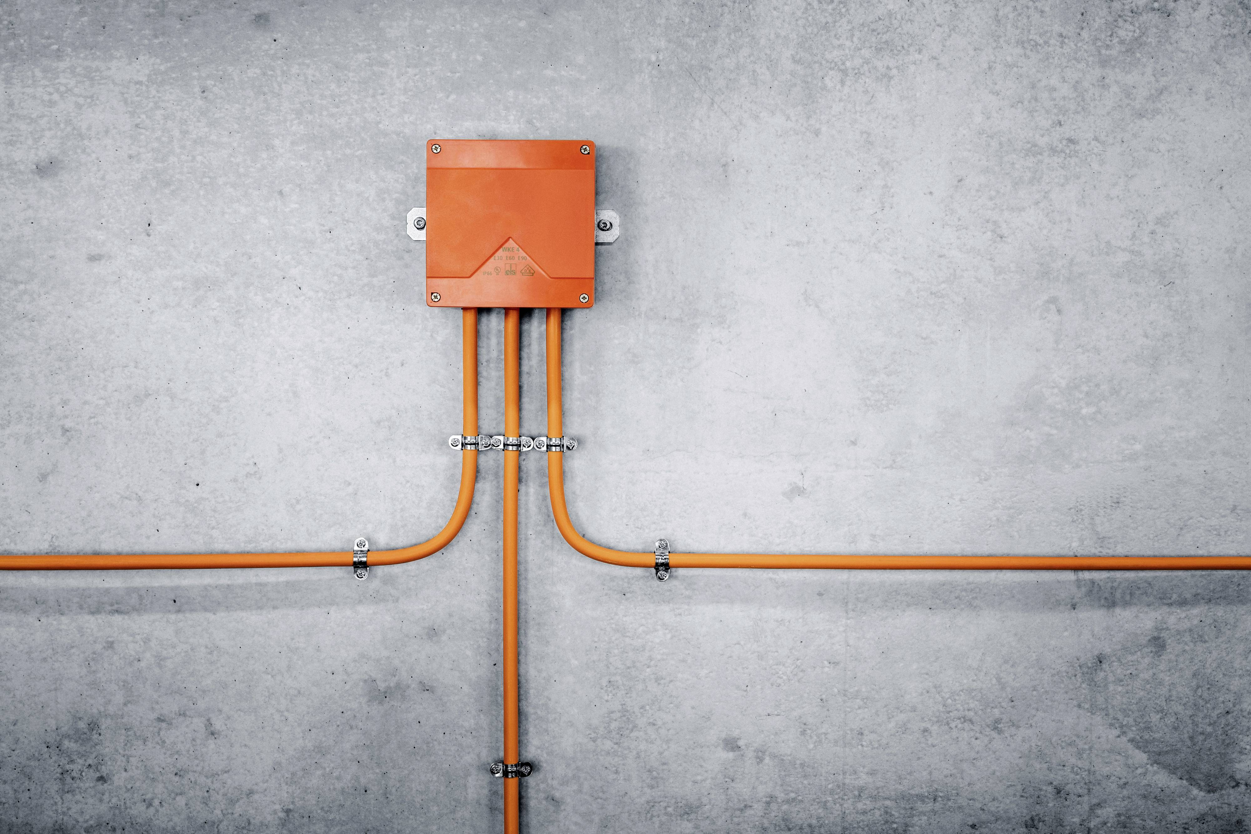 Orange cable box on a grey concrete wall with cables extending to the left and right.