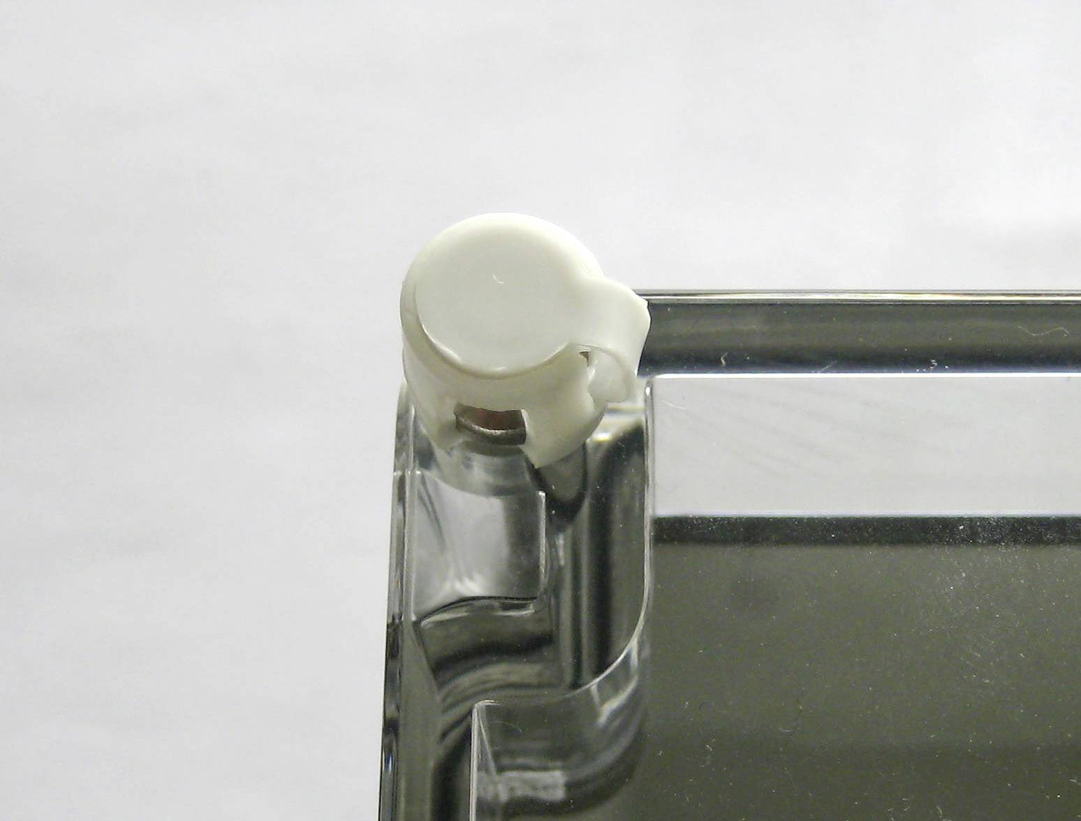 Close-up of a transparent plastic component with a white, round element in the corner, against a neutral background.