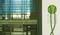 A green power plug hangs from a white socket next to a window with partially drawn venetian blinds, with a scaffolding in the background.