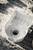 A white plastic component lies on stony ground. It has a circular opening in the centre and a textured inner surface.