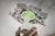 A hand holds a white plastic cylinder beneath a hole in a ceiling with crumbling concrete. The hole has a green background.